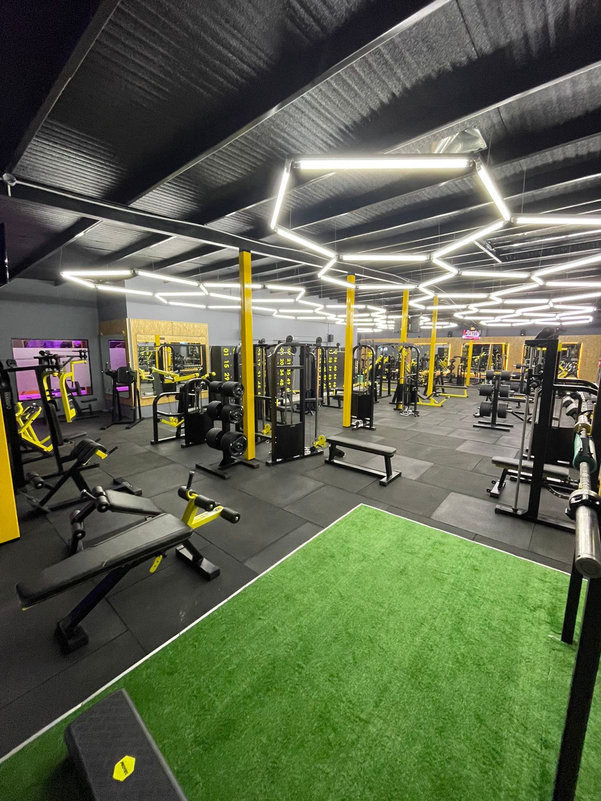 Interior del gimnasio TERRA FITNESS en Ituzaingó, piso de goma negro y luces LED hexagonales amarillas